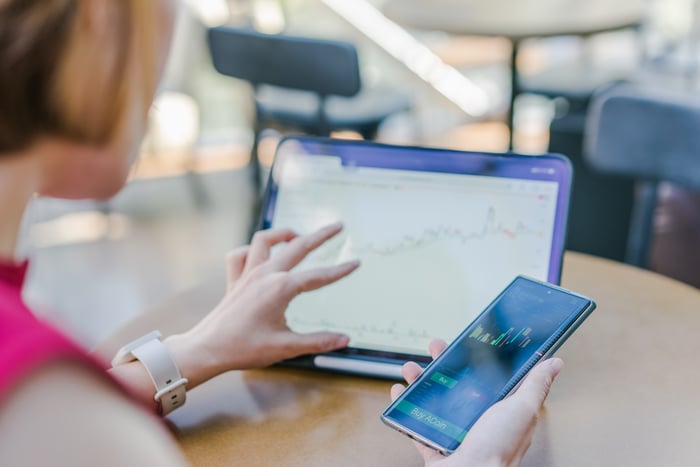 Woman taps graph on tablet while holding cellphone.