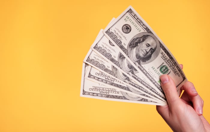 Person holding hundred dollar bills against a yellow background.
